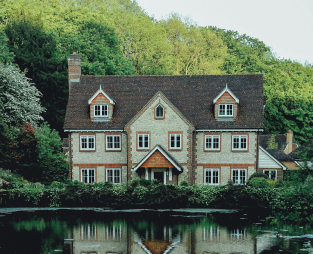 A big house infront of a lake and a forest behind